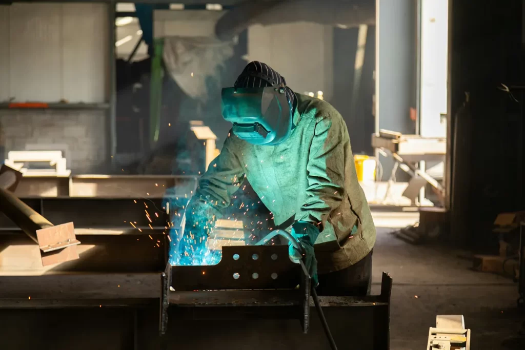 Welder fusing metal in a busy workshop, showcasing the skilled craftsmanship central to Welder / Fabrication jobs Glasgow.