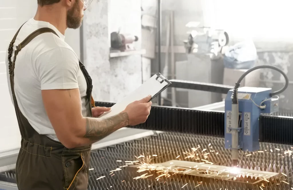 Engineer inspecting work with clipboard while CNC machine cuts metal, representing skilled CNC's jobs in manufacturing.